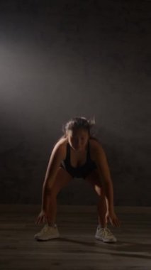 Karanlık bir spor salonunda burpee yapan bir kadın. Fitness ve egzersiz motivasyon ve kararlılık konsepti.