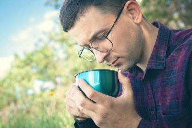 Elinde çay olan genç bir adam. Bir erkek doğada dinlenir. Parkta aktif eğlence