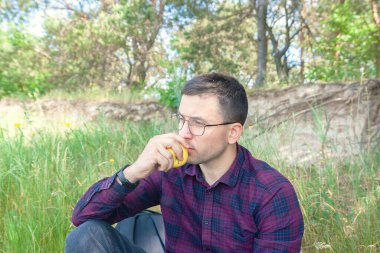 Bir adam ormanda bir elmayla oturuyor. Ormanda turist istirahatı. Doğada aktif eğlence.