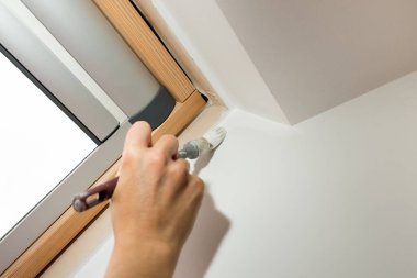 Brush painting the window recess of the sloping roof window with white paint