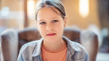 Güzel genç bir kız rahat bir koltukta oturuyor ve doğrudan kameraya bakıyor.