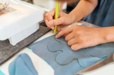 Dikiş makinesinde çalışan kadın ellerini kapat. O, masada oturuyor ve yeşil kalemle çizim yapıyor. Çocuklar için yaratıcı terzilik atölyeleri - kavram