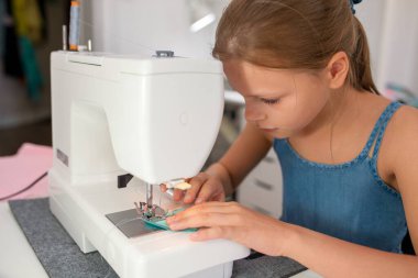 Bir kumaş parçasını dikmek için dikiş makinesi kullanan küçük bir kız. Çocuklar için yaratıcı terzilik atölyeleri - kavram
