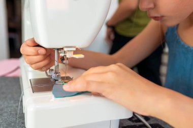 Bir kumaş parçasını dikmek için dikiş makinesi kullanan küçük bir kız. Çocuklar için yaratıcı terzilik atölyeleri - kavram