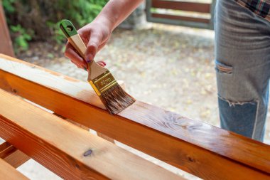 Kapalı alan yenileme projesi sırasında bir işçinin el yapımı ahşap bir yüzeyi fırça ve lekeyle boyaması.