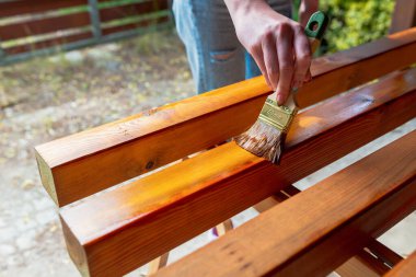 Kapalı alan yenileme projesi sırasında bir işçinin el yapımı ahşap bir yüzeyi fırça ve lekeyle boyaması.