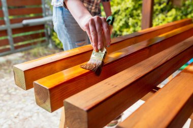 Kapalı alan yenileme projesi sırasında bir işçinin el yapımı ahşap bir yüzeyi fırça ve lekeyle boyaması.