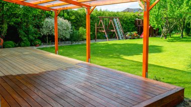 Kapalı terasta, ahşap bir güvertenin yakın çekimi, bir ev geliştirme projesi sırasında yıpranmış ve ahşabı tedavi eden yarı lekeli bir yüzey ile restorasyon sürecini gösteriyor. 