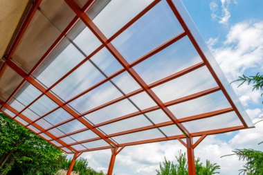 Arka bahçedeki modern ahşap pergola yapının şeffaf polikarbonat çatısı, temiz bir arka plan ile gölge ve koruma sağlıyor..