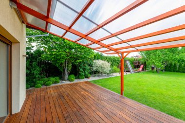Çağdaş arka bahçedeki bahçe güvertesini kaplayan şeffaf polikarbonat çatılı ahşap pergola.