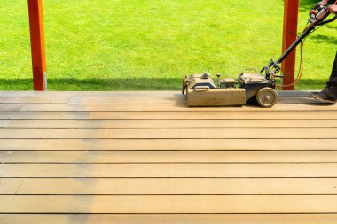 İşçi, arka bahçede özel bir makineyle ahşap bir güverteyi temizleyip zımparalıyor.