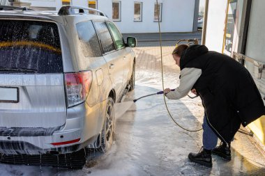 Kadın oto yıkamada kirli bir SUV 'u temizlemek için yüksek basınçlı çamaşır makinesi kullanıyor.