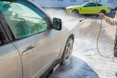 Bir SUV 'u yüksek basınçlı su ve köpükle yıkamak self-servis araba yıkama, güneşli bir günde aracın dışını temizlemek.