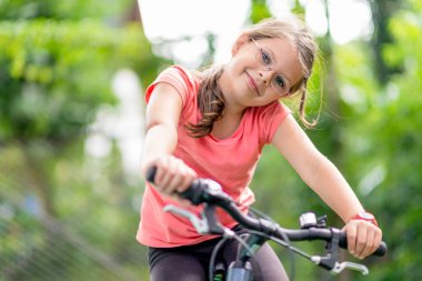 Yeşil bir parkta bisiklet süren gözlüklü genç bir kız aktif bir yaşam tarzı ve yaz tatilinin tadını çıkarıyor.