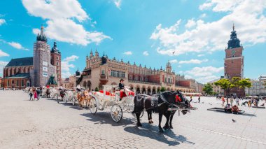 Krakow, Polonya - 29 Temmuz 2024; St. Mary Bazilikası ile Krakow Ana Meydanı 'nda at arabaları ve Blue Sky' ın altında Kumaş Salonu