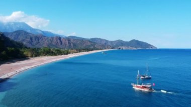 Akdeniz 'de Antik Olimpos yakınlarında iki yat ısınıyor. Fotoğrafta Takhtala dağları, mavi deniz ve kumlu bir sahil görünüyor..