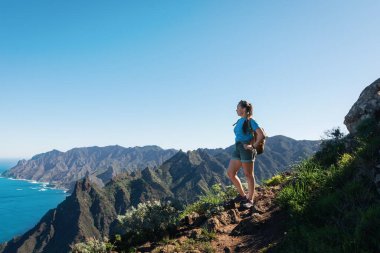 Sırt çantalı bir kız, Anaga Dağları 'nda yürüyüşe çıkar ve güzel kostüm manzarası izler. - Tenerife, Kanarya Adaları, İspanya. sahil görünümü