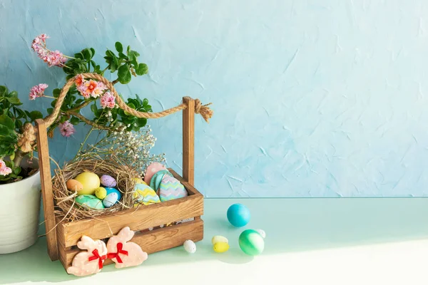 Masada paskalya yumurtası ve tatlı olan ahşap sepet. Saksıda çiçekler olan sıradan bir mutfak odası. Paskalya konsepti.