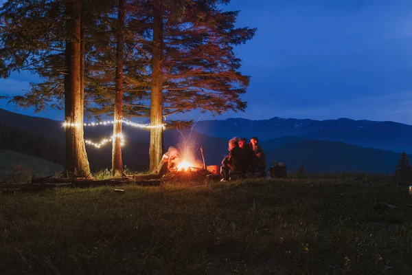 A group of tourists sits around a campfire at a campsite. Lights and night in the mountains.