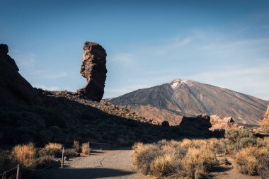 Güneşli bir günde arka planda ünlü Pico del Teide volkanı zirvesi olan Roque Cinchado kaya oluşumunun panoramik görüntüsü, Teide Ulusal Parkı, Tenerife, Kanarya Adaları