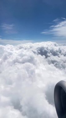 Bir uçağın yolcu penceresinden mavi gökyüzüne karşı kalın bulutlara, dikey görüntülerName.