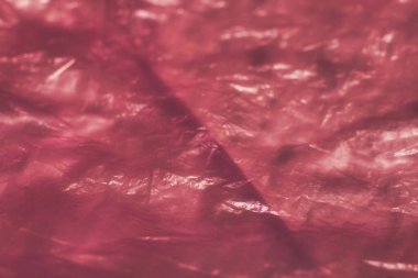 Kırışık ve kıvrımları gösteren buruşuk pembe plastik dokuların yakın çekimi. Resim, arka plan, doku ve soyut temalar için uygun hale getirerek yansıtıcı yüzey ve karmaşık desenleri vurgular.