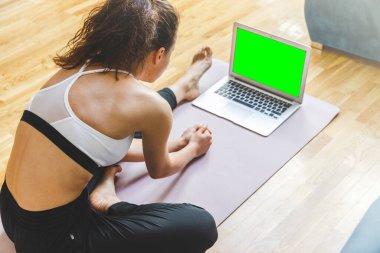 Arkadaki kadın evde yoga egzersizi yapıyor. Bilgisayarını ve online dersini kullanıyor..