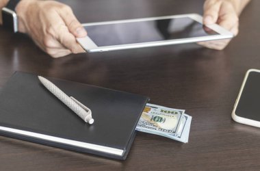 Masadaki defterde dolar banknotları, ellerinde dijital tablet.