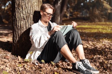 Genç kısa saçlı kadın parkta oturmuş kitap okuyor..