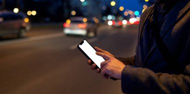 Mobile phone with blank screen in male hand in city at night.