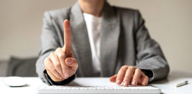 Female person sitting at the desk working on computer touching virtual screen with finger.