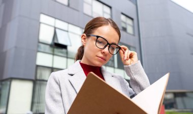 Gözlük takan tesis müdürü kadın açık alanda ofis binasının yanında duruyor..