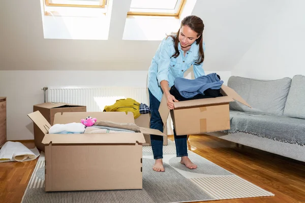 Woman packing her clothes in cardboard boxes, moving house concept.