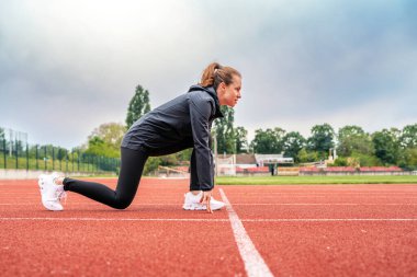 Spor yaparken koşu pistinde başlangıç pozisyonunda koşan genç kadın koşucu.