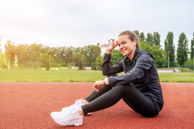 Sporcu genç bayan koşucu antrenmandan sonra koşu pistinde dinleniyor ve gülümsüyor..