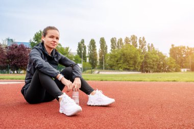 Atletik kadın koşucu antrenmandan sonra koşu pistinde oturup dinleniyor..