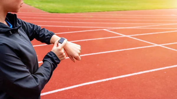 stock image Woman athlete runner standing on running tracks and using her digital wrist watch.