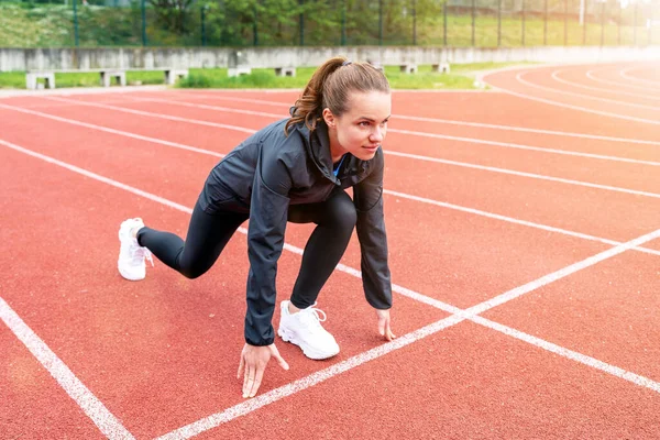 stock image Brunette woman runner in start position on running track while workout.