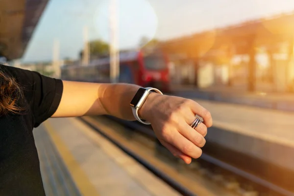 Digital wrist watch on female hand and defocuset train and railway platform on background.