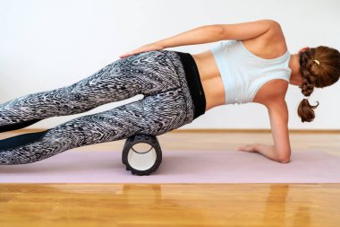 Slim sportif dişinin gerilmek ve bacak kaslarının esnekliğini arttırmak için fitness köpük silindiri kullanmasının arka plan görüntüsü.