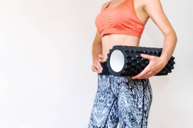 Beyaz arka planda duran ve elinde köpük silindiri tutan tanınmamış bir bayan sporcu..