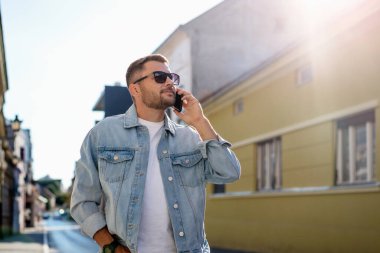 Avrupa 'nın caddesinde yürürken konuşan şık kot ceketli ve güneş gözlüklü yakışıklı genç adam..