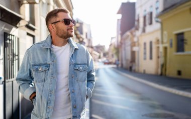 Güneş gözlüklü ve kot ceketli yakışıklı, genç bir esmer şehirde dolaşıyor..