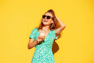 Yazın yeşil çimenli ve gözlüklü çekici esmer kadın sarı arka planda poz veriyor ve gülüyor..