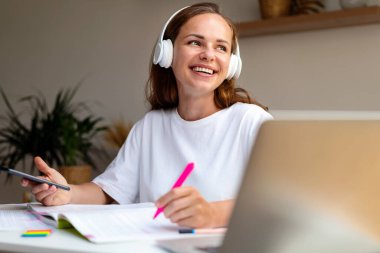 Genç kız üniversite öğrencisi, kablosuz kulaklığı ve akıllı telefonuyla eğitici ses kayıtlarını dinliyor..