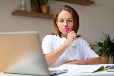 Genç bir kadın internet üzerinden ev ödevi yapıyor, bilgisayarını ve çalışma kitabını kullanıyor, evden uzaktan eğitim alıyor..