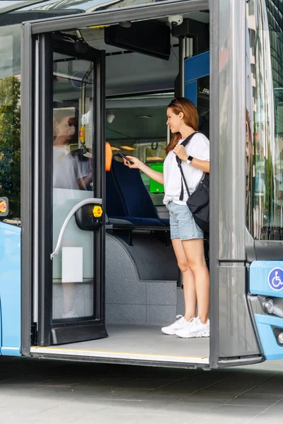Woman passenger of public transportation in city pays for bus using her smart phone.