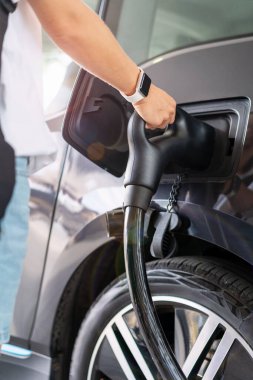 EV yükleniyor. Kadın eller arabanın elektrikli şarj aletini tutuyor.