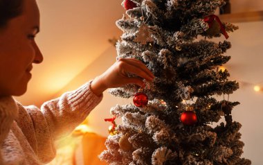 Sıcak yün kazak giyen mutlu kadın evdeki Noel ağacını süslüyor..
