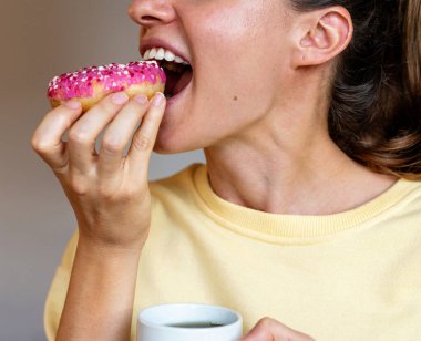 Gülümseyen kadın pembe renkli donut yiyor..